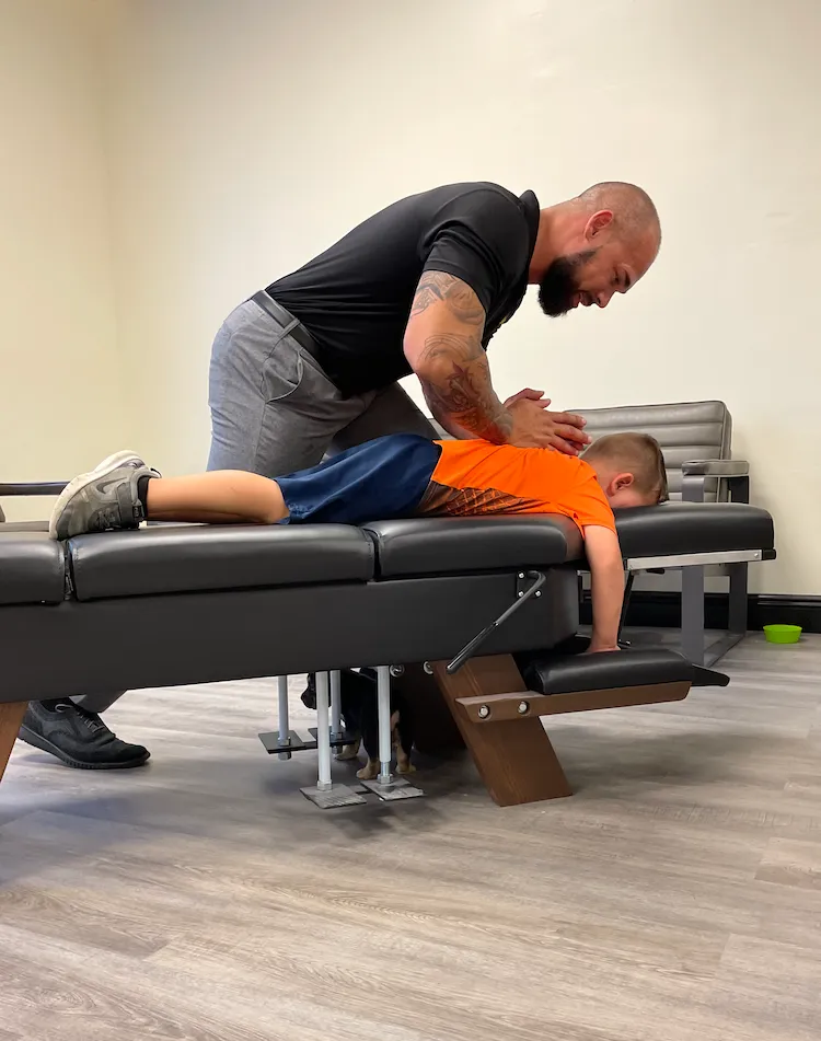 Dr. Junior adjusting the back of a young boy lying face down on a drop table.