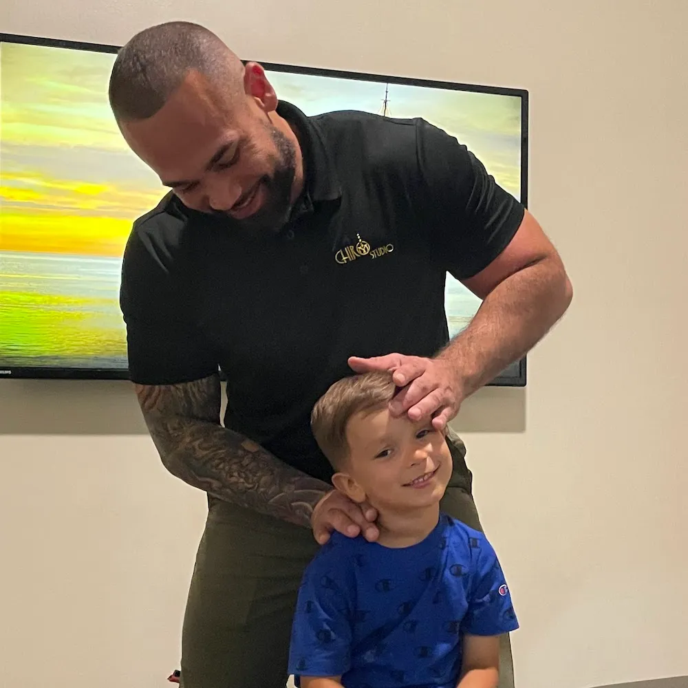 Dr. Junior smiling as he places his hands on a young boy’s head to check his neck.