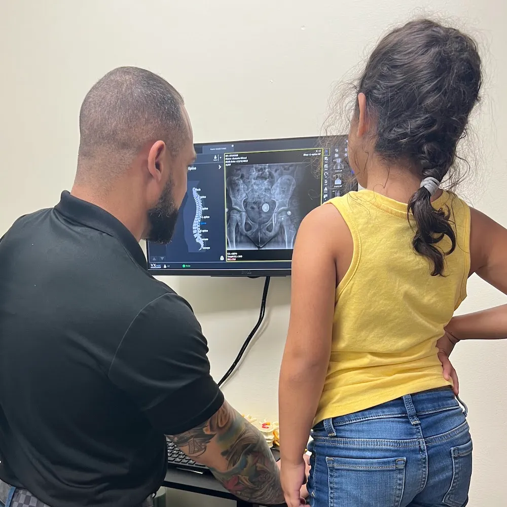 Dr. Junior showing a young girl a spinal X-ray on a computer monitor.