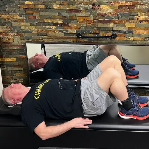 Older man in a Chiro Studio T-shirt lying face up on a treatment table with his knees bent.