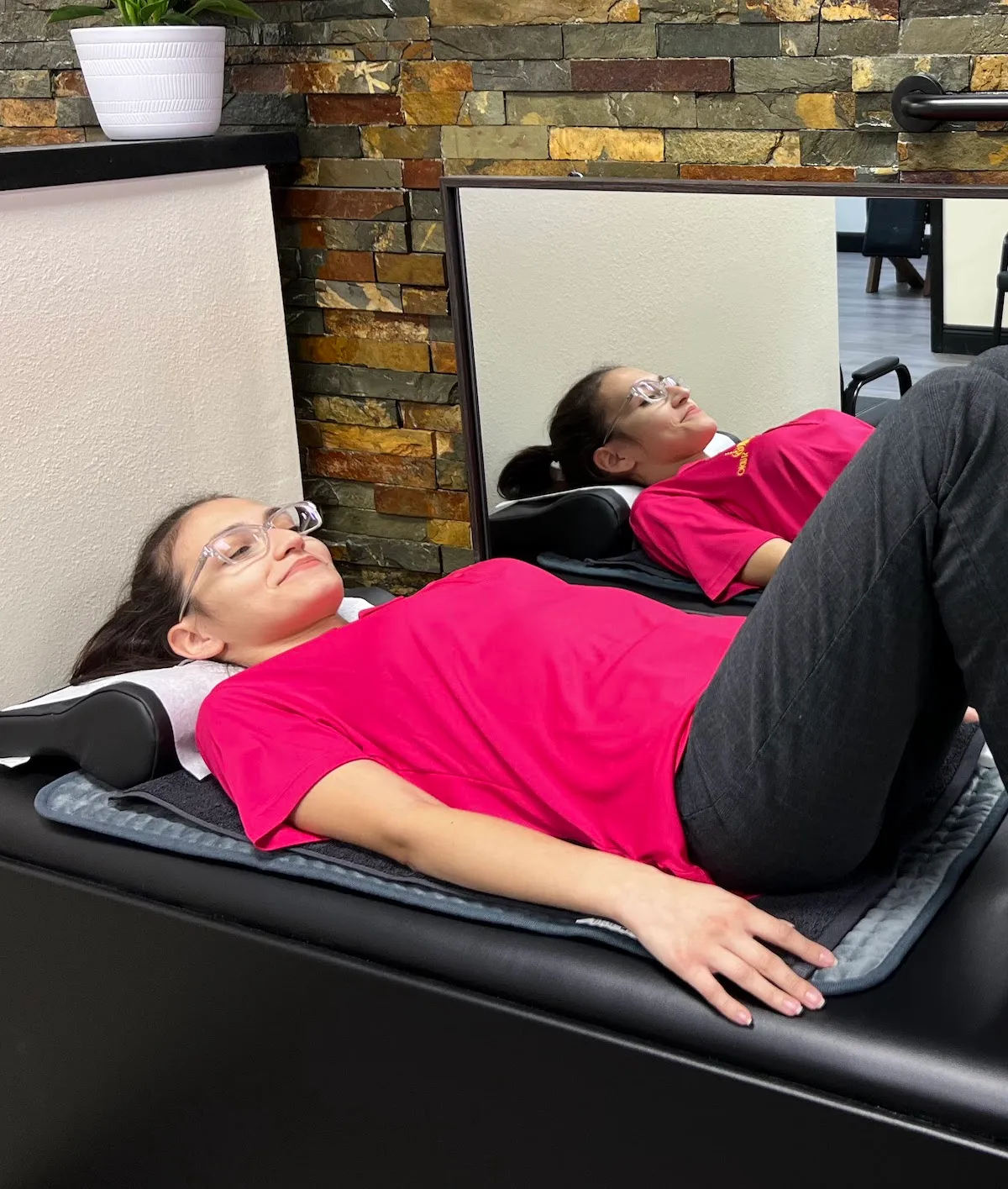 Young woman in glasses and a pink shirt lying face up on a padded treatment table.