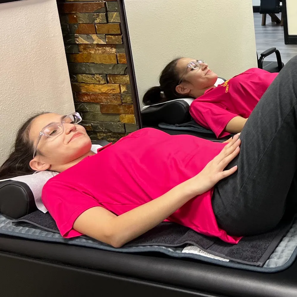 Young woman in a pink shirt relaxing face up on a padded therapy table.