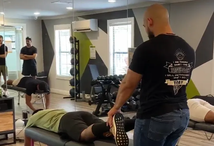 Chiropractor stretching the leg of an athlete lying face down on a table in a gym.
