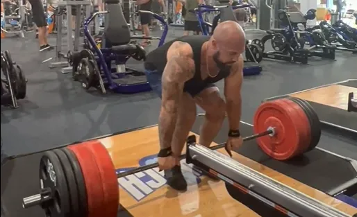 Dr. Junior gripping a loaded barbell for a deadlift at the gym.