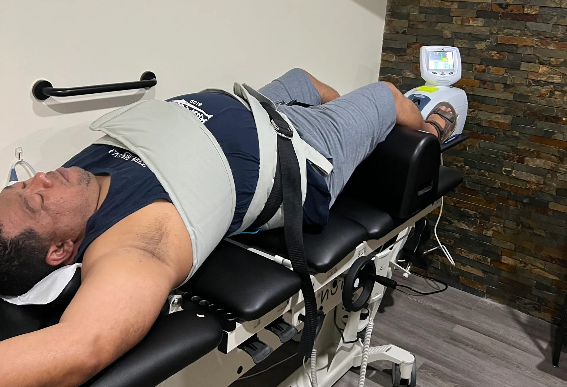 Male patient strapped into a spinal decompression table with his legs on a knee support.