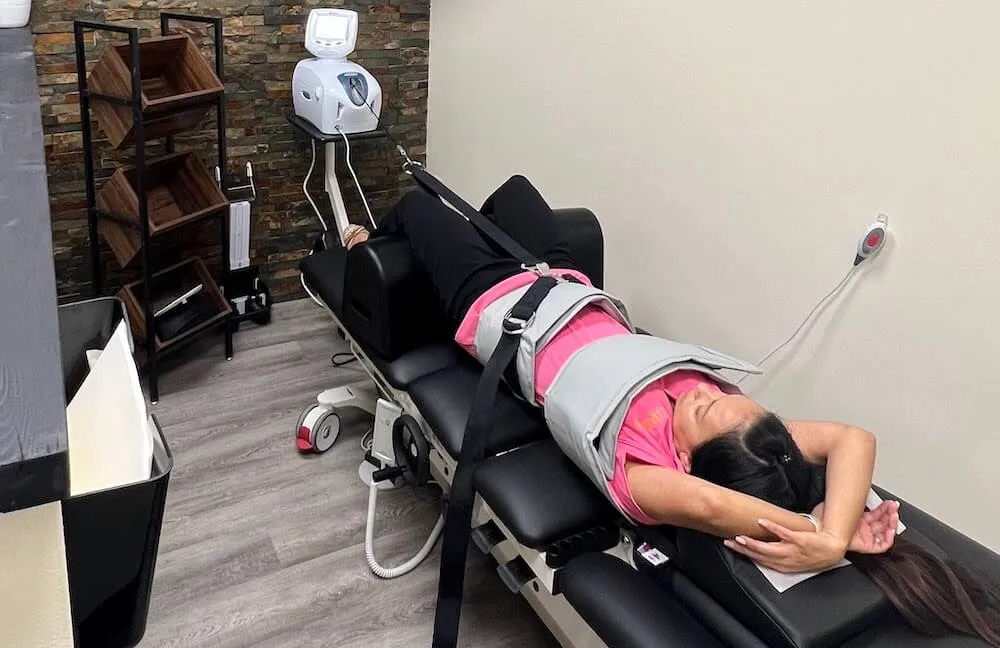 Woman in a pink shirt strapped into a spinal decompression table with her arms behind her head.