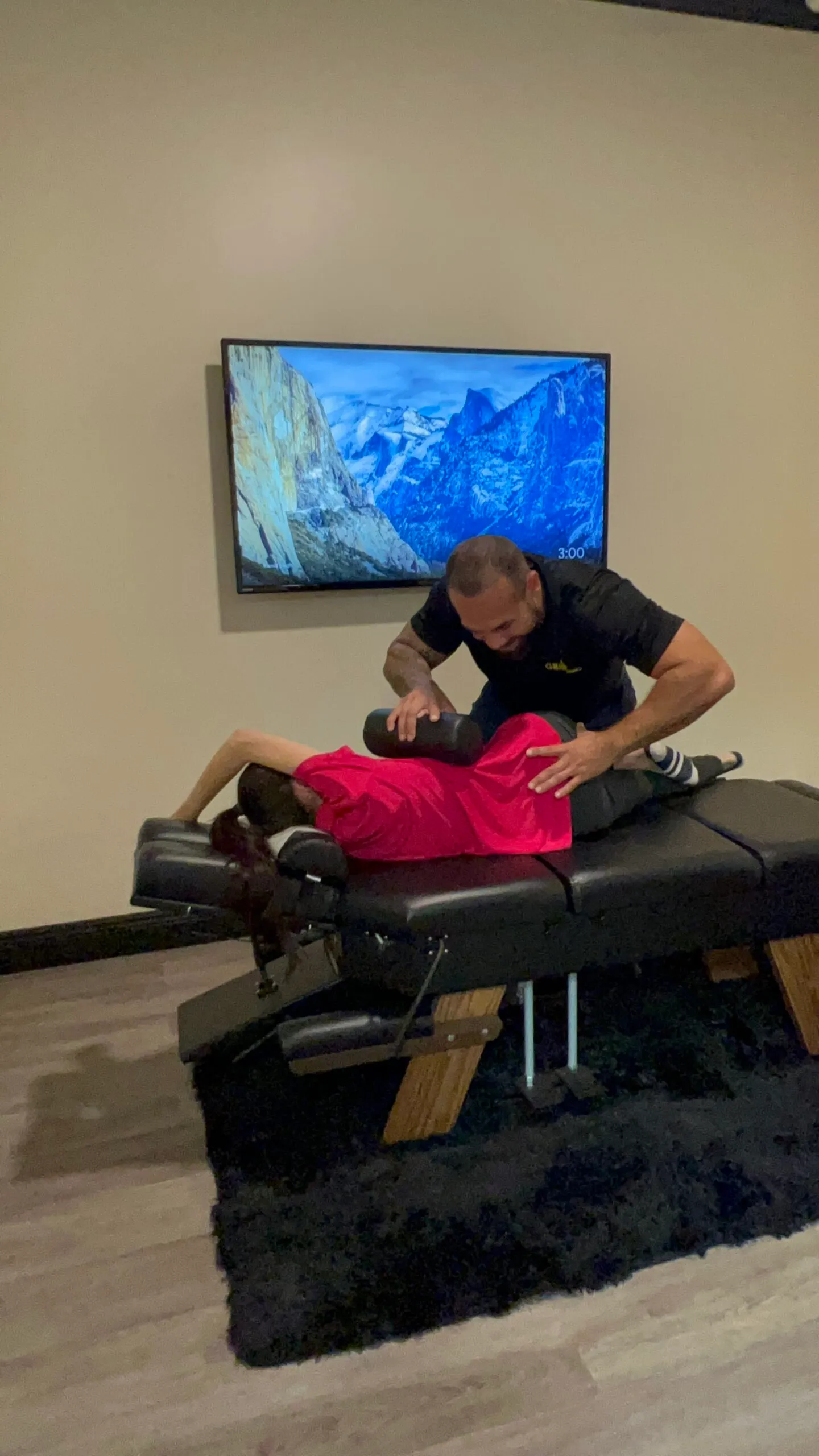 Dr. Junior using a bolster to perform a side-lying adjustment on a woman in a pink shirt.