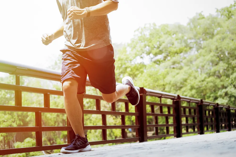 Runner in shorts and sneakers jogging across a park bridge.