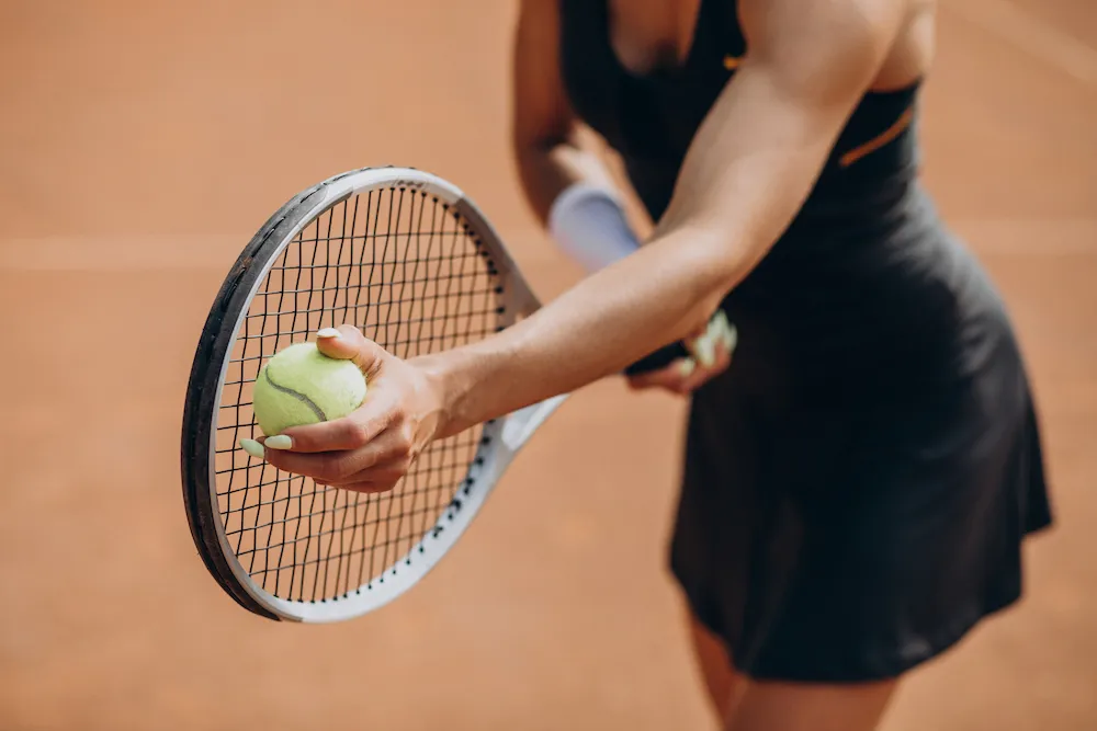 Tennis player holding a ball against her racket as she prepares to serve.
