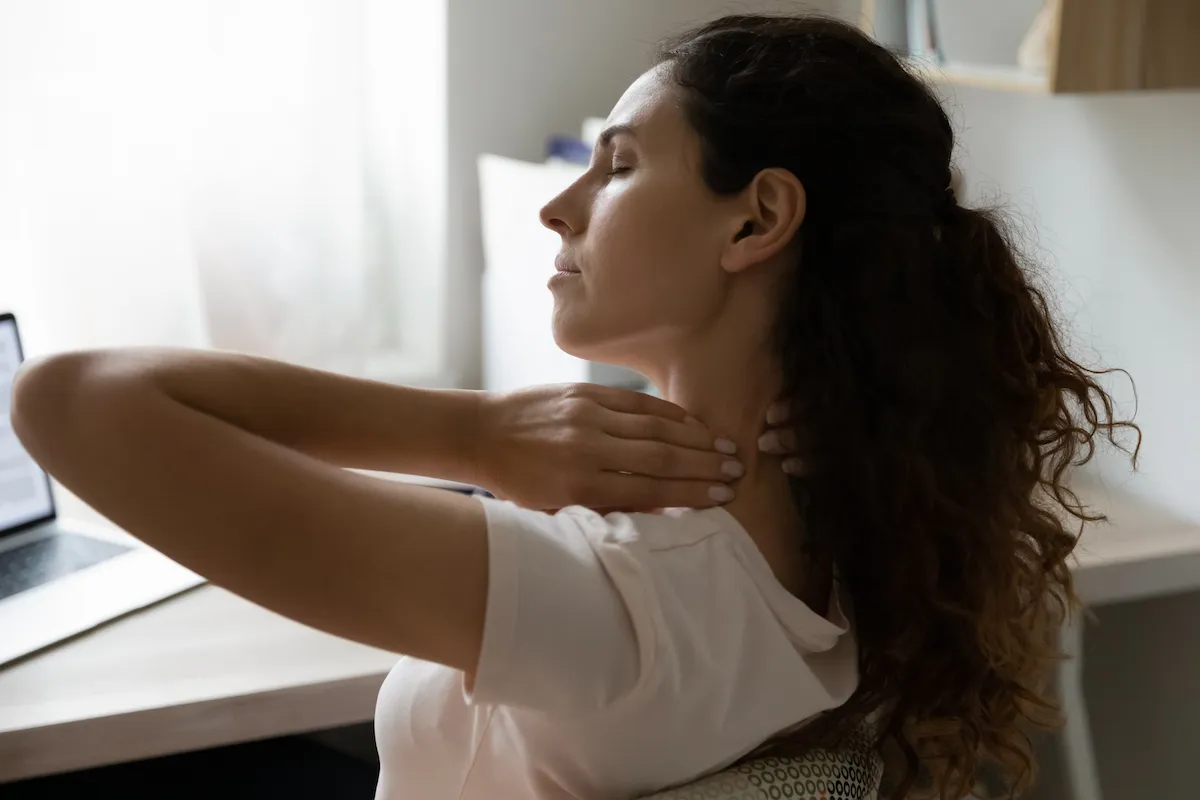 Woman with eyes closed rubbing her stiff neck while working at a laptop.